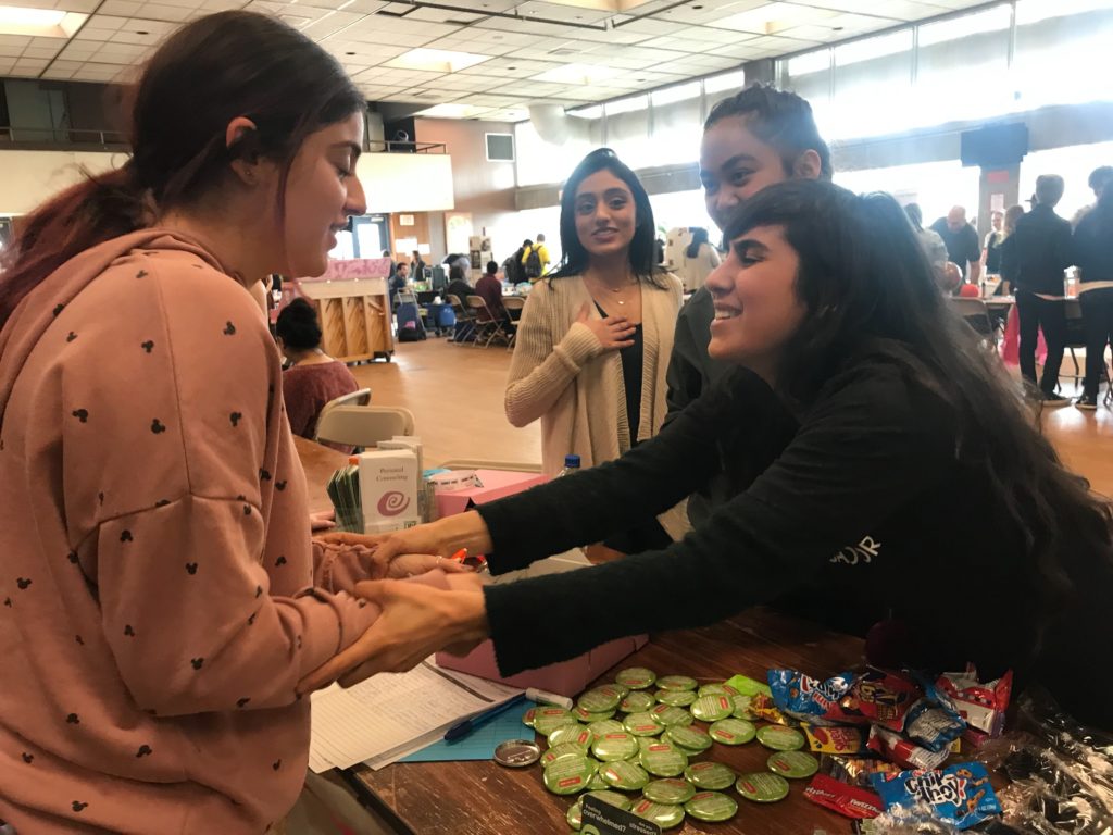 Student Wellness Ambassadors greet a fellow student across an event table